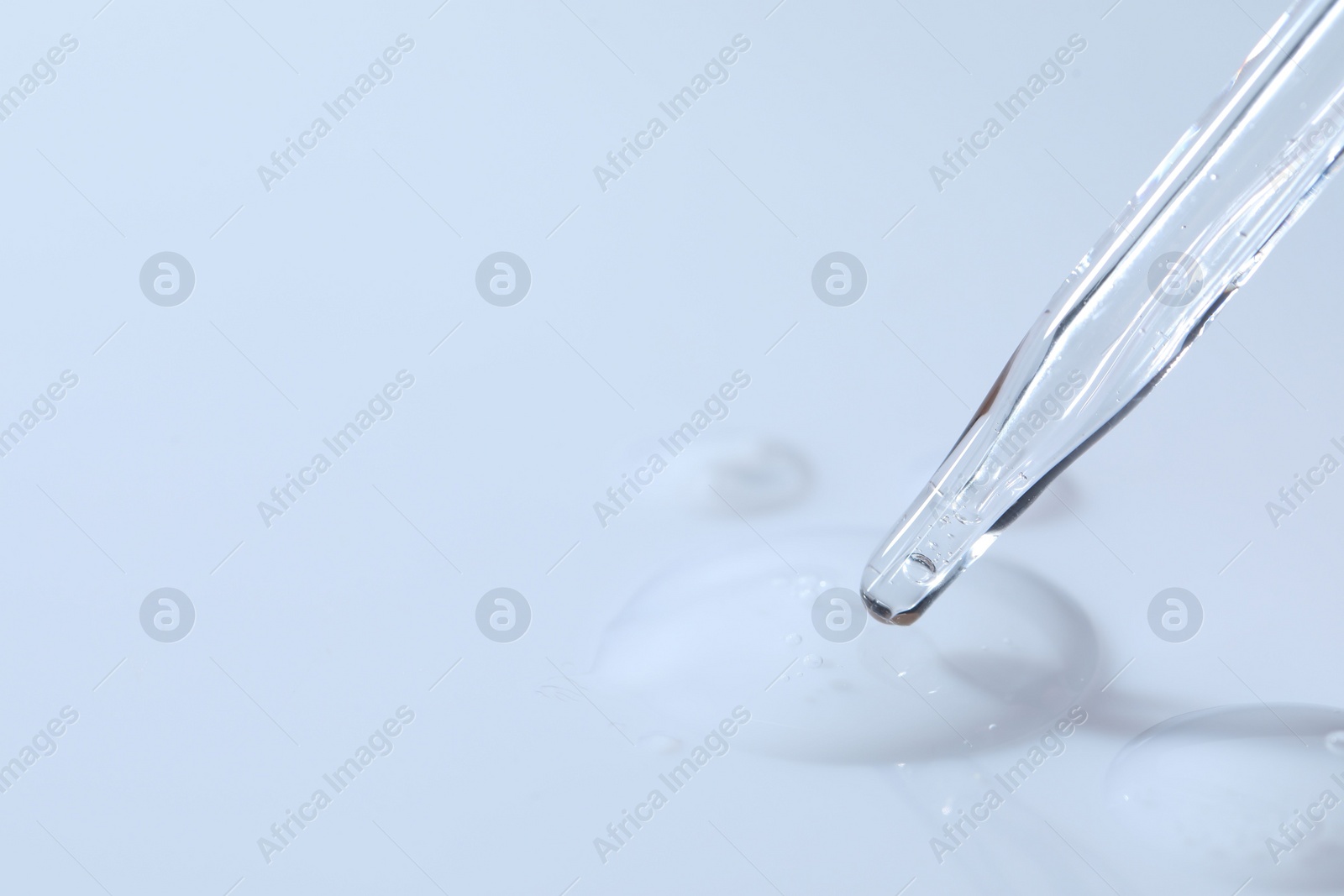 Photo of Glass pipette and transparent liquid on white background, closeup. Space for text