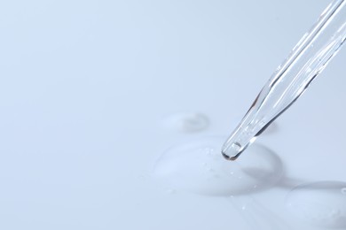 Photo of Glass pipette and transparent liquid on white background, closeup. Space for text