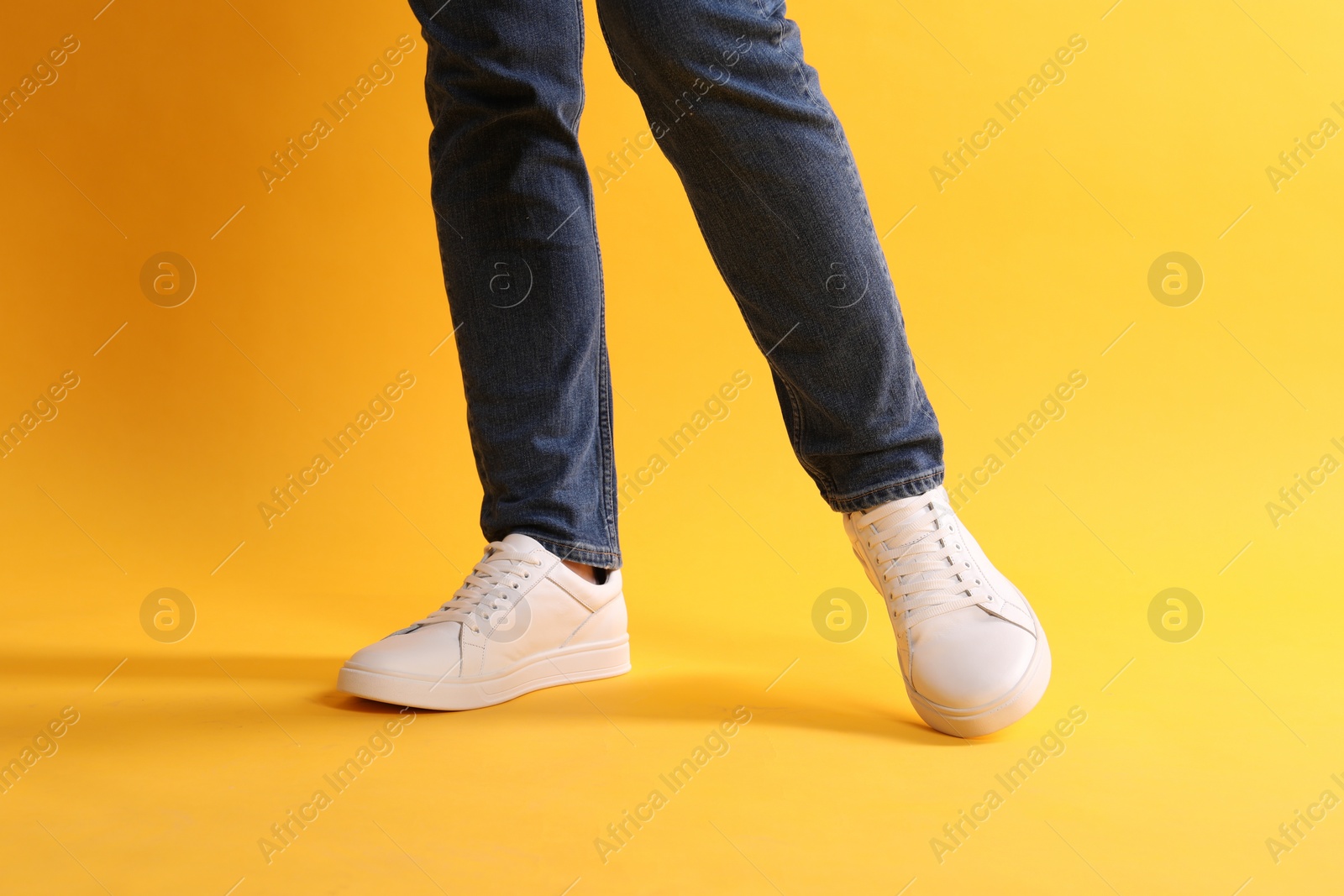 Photo of Man wearing stylish white sneakers on yellow background, closeup