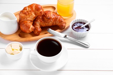 Photo of Fresh croissants, butter, jam and coffee on white wooden table. Tasty breakfast