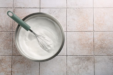 Bowl and whisk with whipped cream on tiled table, top view. Space for text