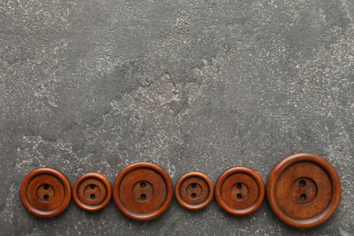 Photo of Brown sewing buttons on grey stone background, flat lay. Space for text