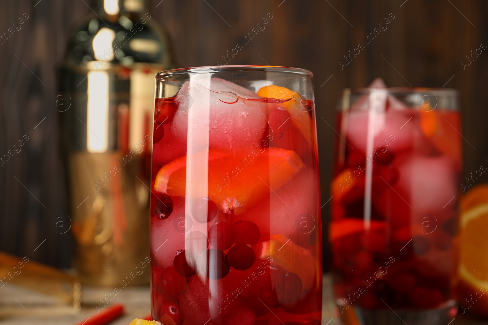 Photo of Tasty cranberry cocktail with ice cubes and orange in glasses on table, closeup