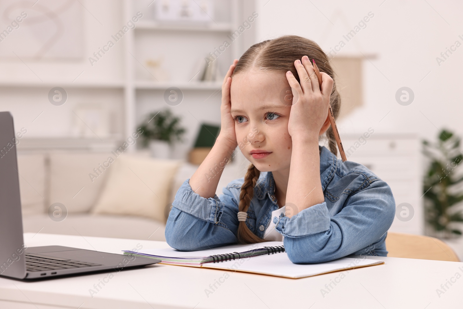 Photo of Little girl suffering from headache while doing homework at home