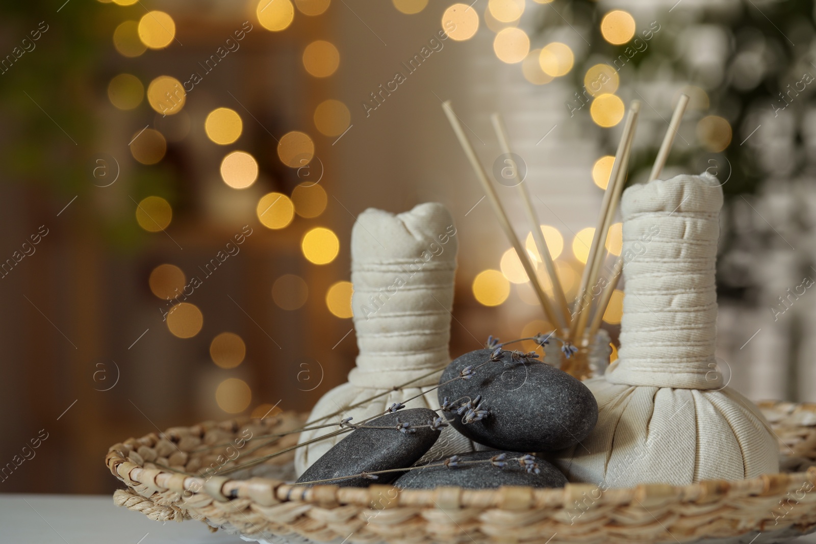 Photo of Spa composition. Herbal bags, stones, reed diffuser and dry lavender flowers on table indoors, bokeh effect