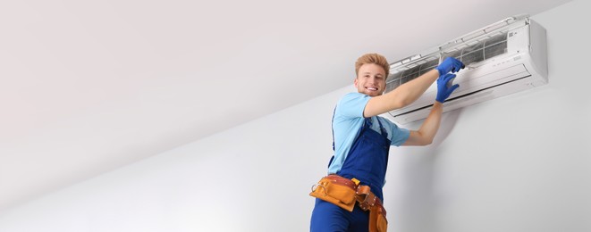 Professional technician checking modern air conditioner indoors, space for text. Banner design