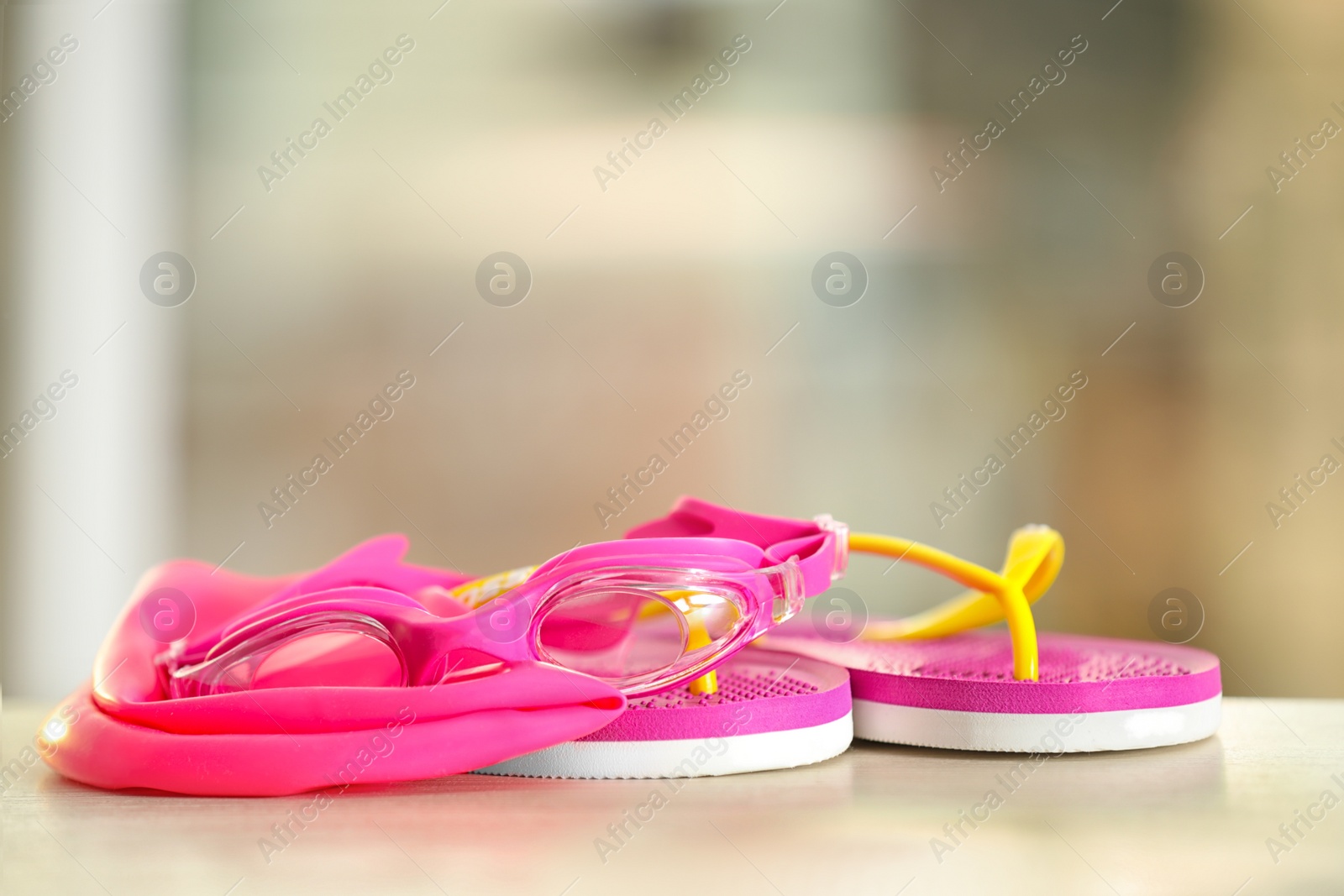 Photo of Swimming cap, goggles and flip flops against blurred background. Space for text