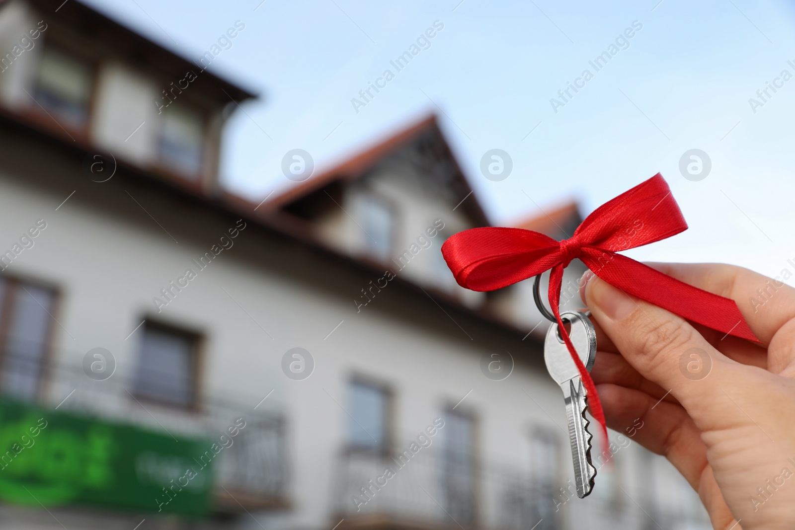 Photo of Woman holding key with bow near house outdoors, closeup. Space for text