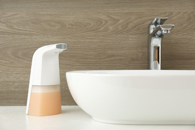 Photo of Modern automatic soap dispenser near sink in bathroom, closeup