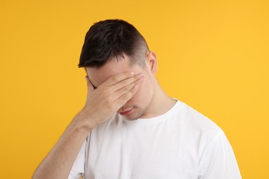 Embarrassed man covering face with hand on orange background