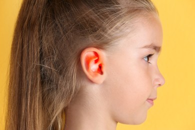 Image of Little girl on yellow background, closeup. Hearing problem