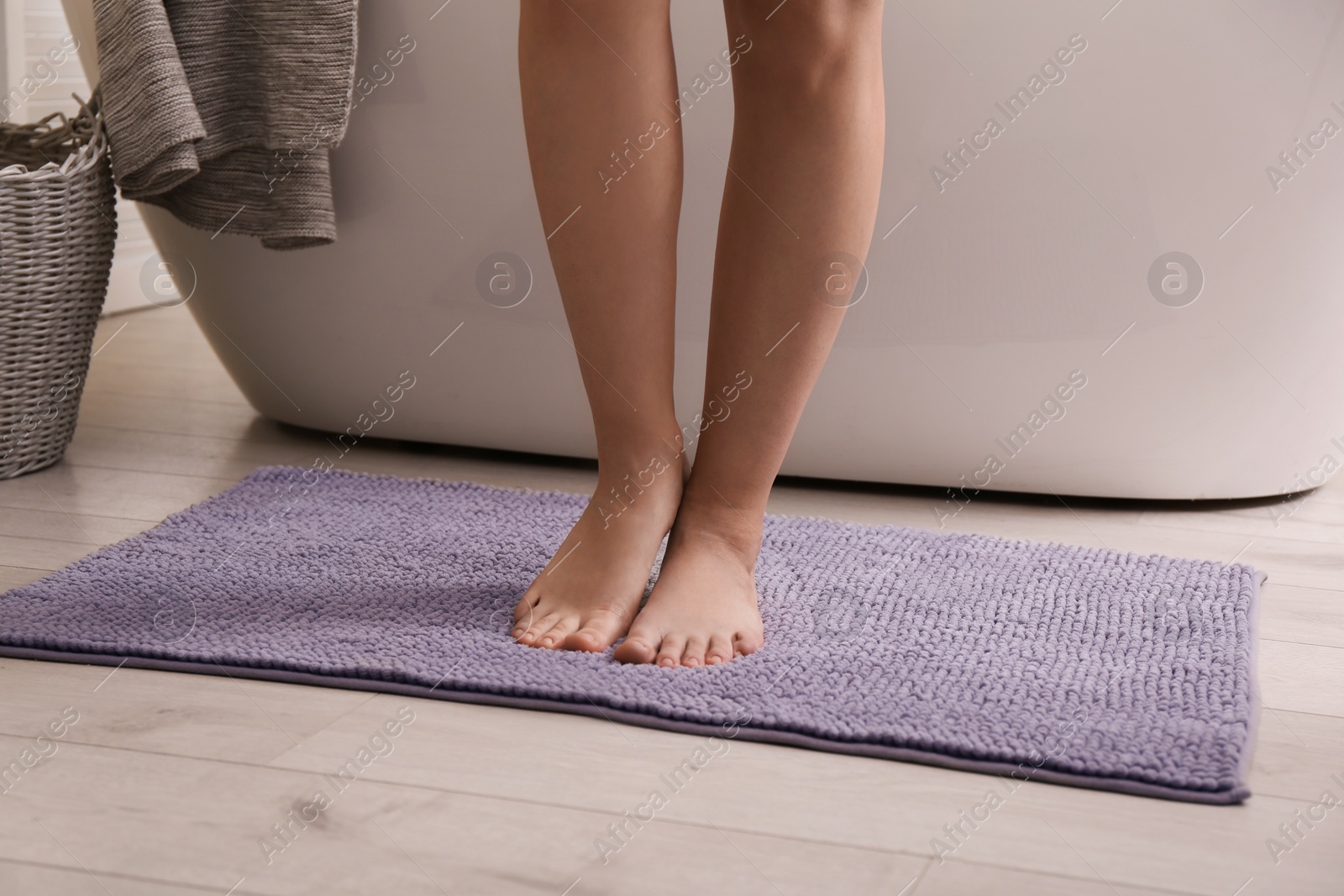 Photo of Woman standing on soft grey bath mat near tub at home, closeup