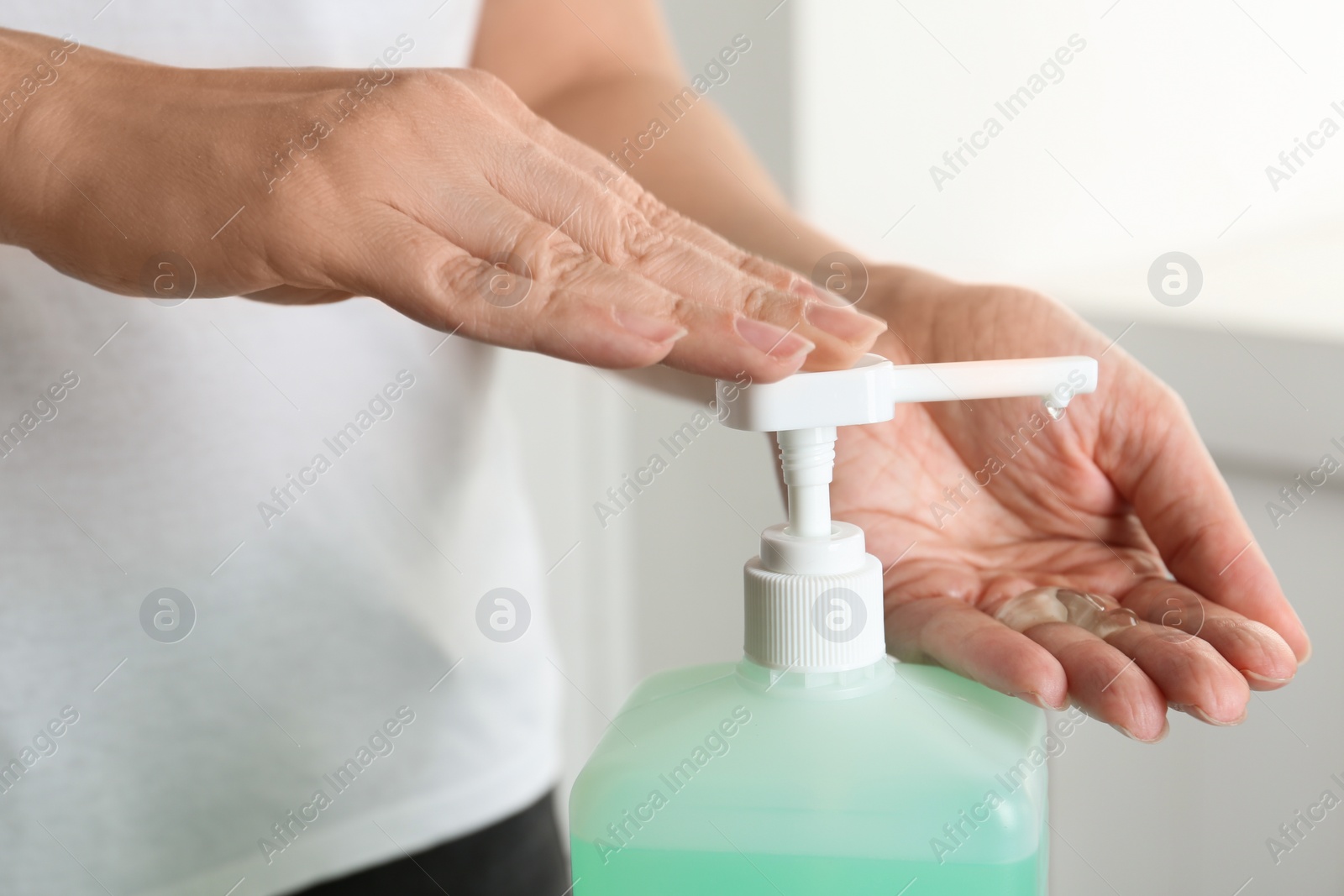 Photo of Woman applying antiseptic gel on hand indoors, closeup