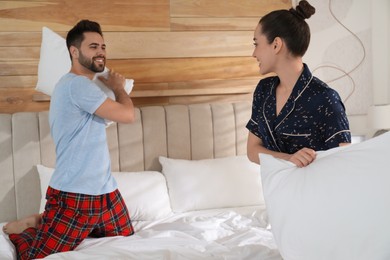 Happy couple in pajamas having pillow fight on bed at home