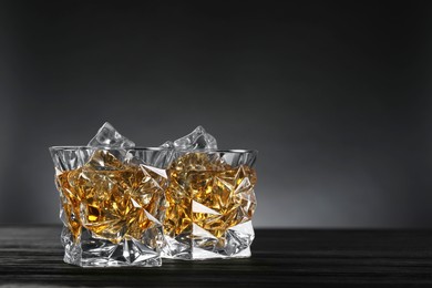 Whiskey and ice cubes in glasses on black wooden table, closeup. Space for text