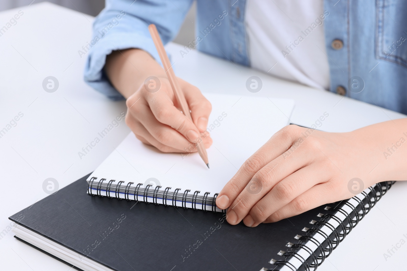 Photo of Young woman drawing in sketchbook at white table, closeup