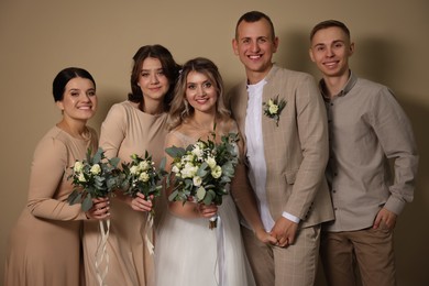Happy newlyweds and their friends on beige background