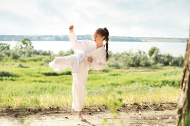 Photo of Cute little girl in kimono practicing karate outdoors