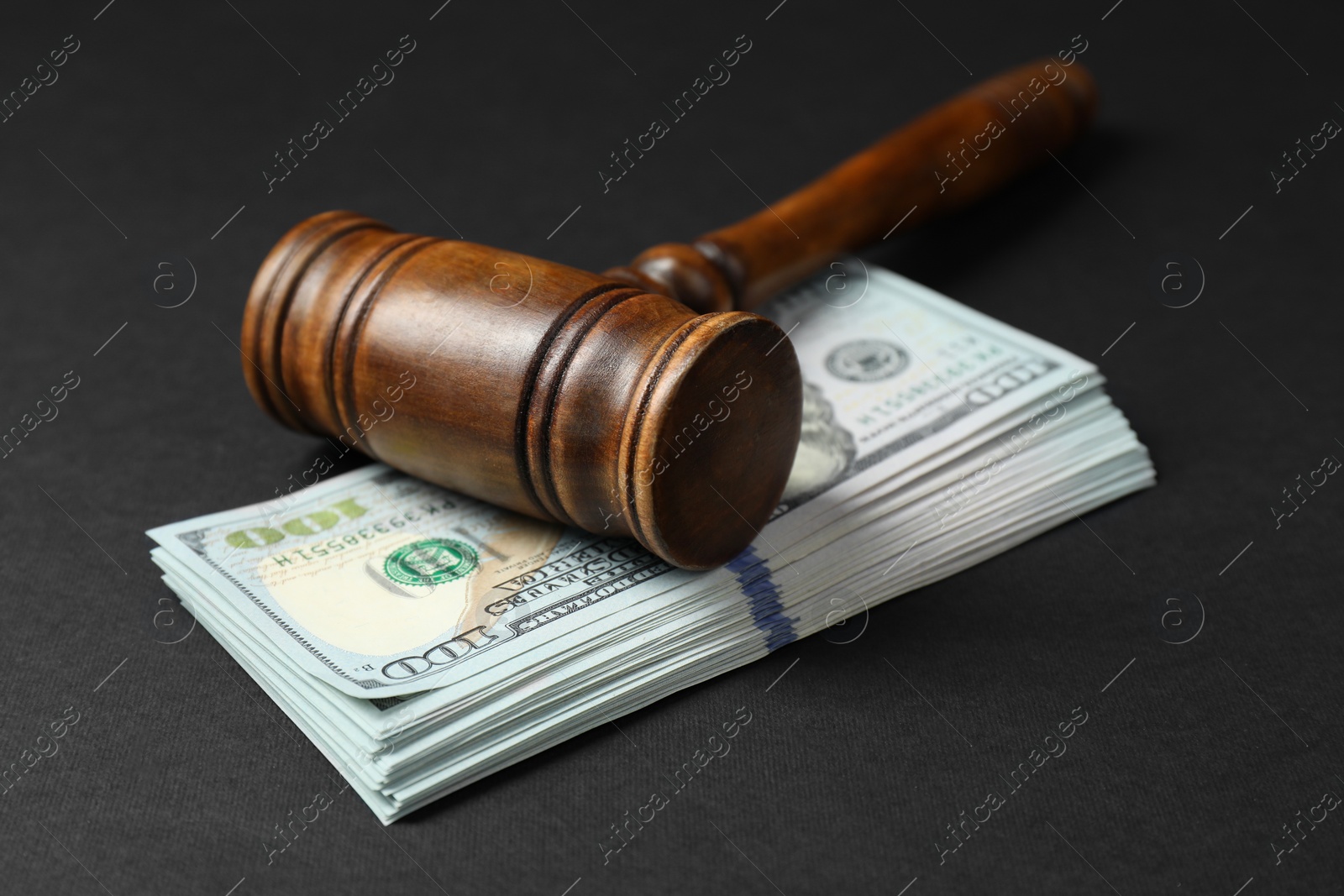 Photo of Law gavel with stack of dollars on black table, closeup