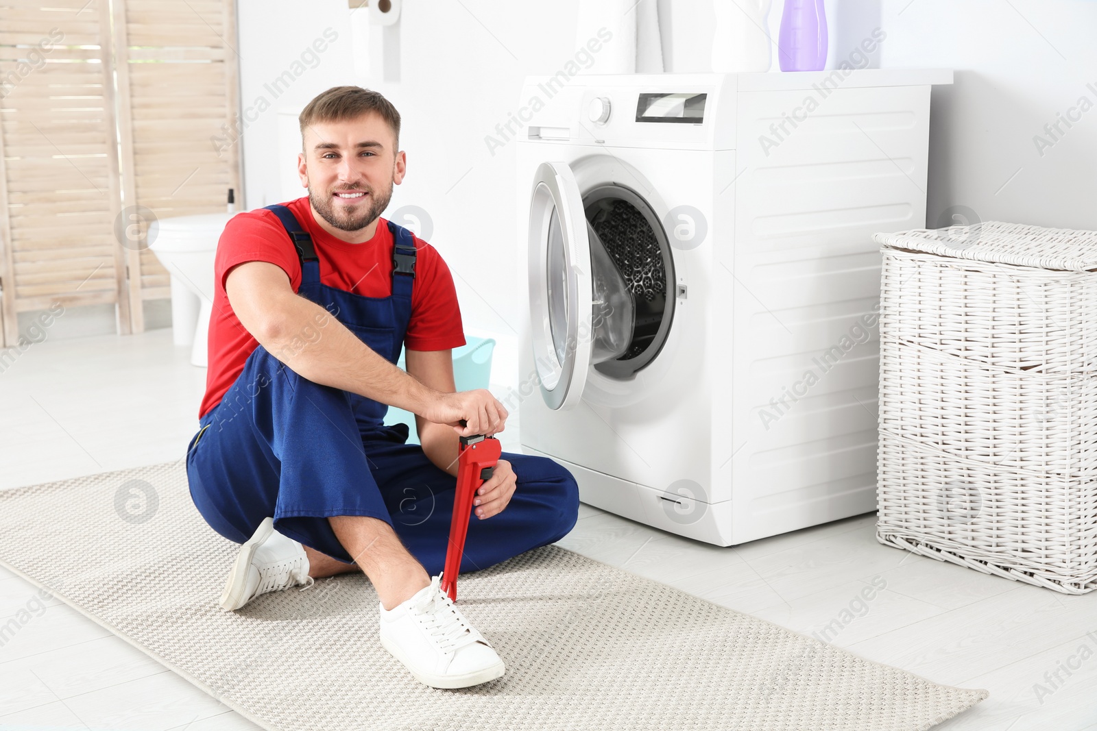 Photo of Young plumber with wrench near washing machine in bathroom