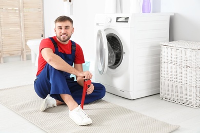 Young plumber with wrench near washing machine in bathroom