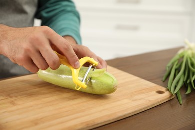 Photo of Man peeling zucchini at kitchen table, closeup. Preparing vegetable