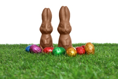 Chocolate bunnies and eggs on green grass against white background. Easter celebration