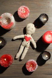 Photo of Voodoo doll with pins in circle of burning candles on wooden table, flat lay