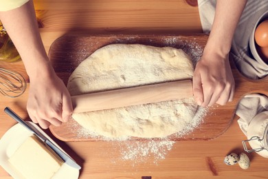 Photo of Woman rolling dough with wooden pin at table, top view