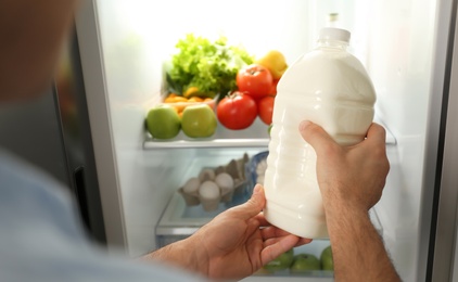 Photo of Man putting gallon of milk into refrigerator indoors, closeup