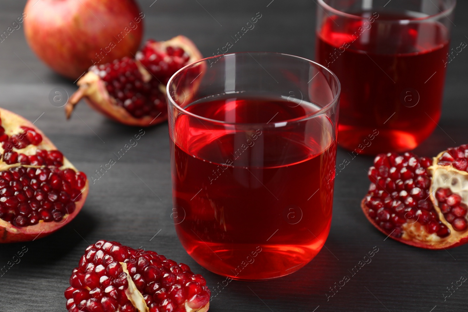 Photo of Tasty pomegranate juice in glasses and fresh fruits on black wooden table, closeup