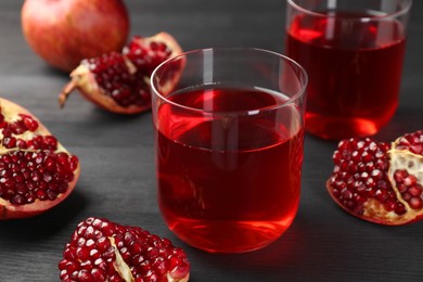 Photo of Tasty pomegranate juice in glasses and fresh fruits on black wooden table, closeup