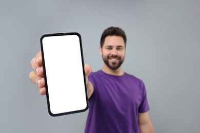 Photo of Young man showing smartphone in hand on light grey background, selective focus. Mockup for design