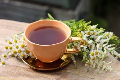 Photo of Cup of delicious chamomile tea and fresh flowers outdoors on sunny day, closeup