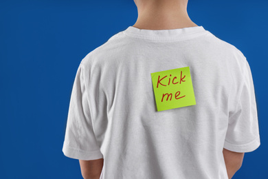 Photo of Preteen boy with KICK ME sticker on back against blue background, closeup. April fool's day