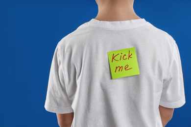 Preteen boy with KICK ME sticker on back against blue background, closeup. April fool's day