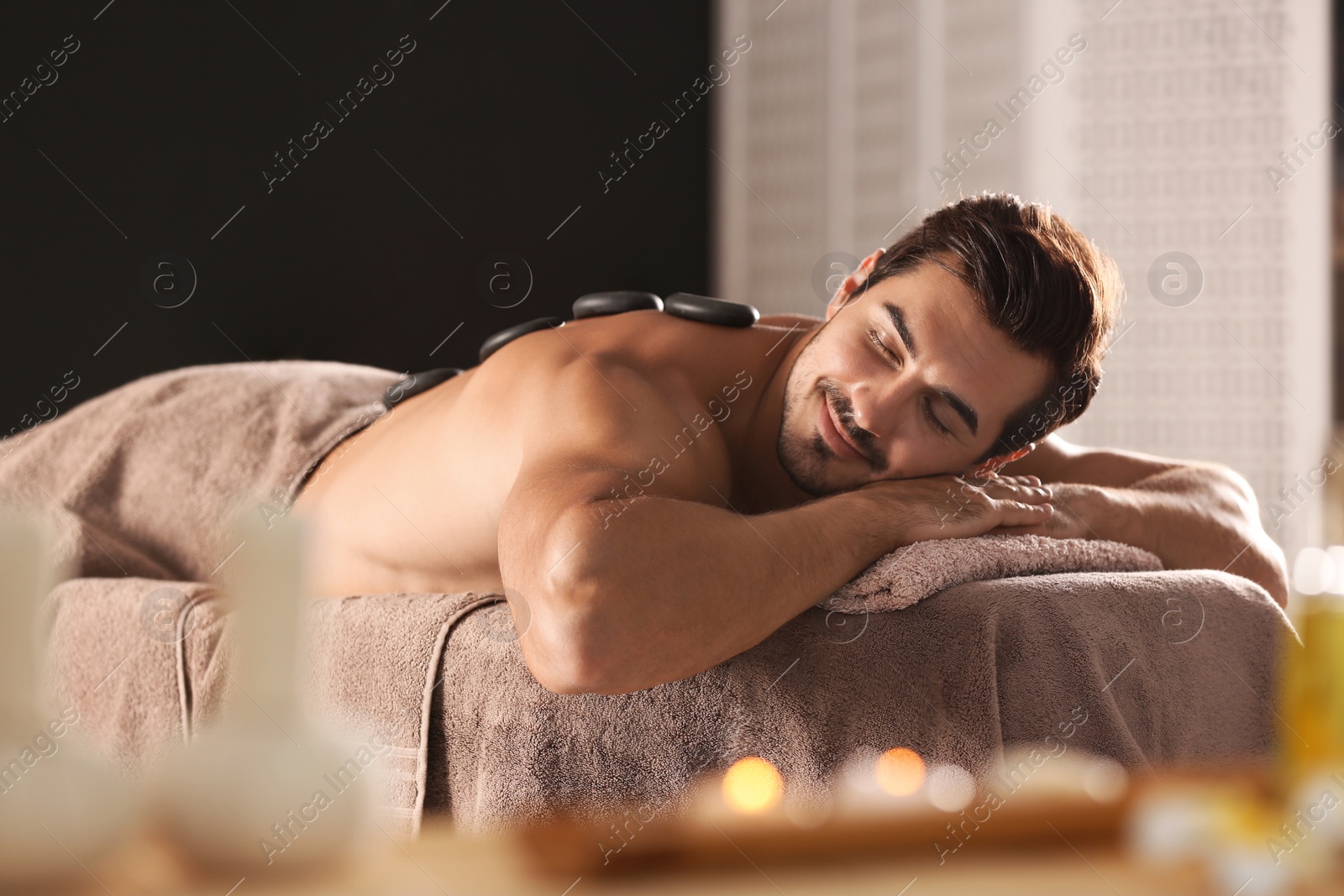 Photo of Handsome young man receiving hot stone massage in spa salon