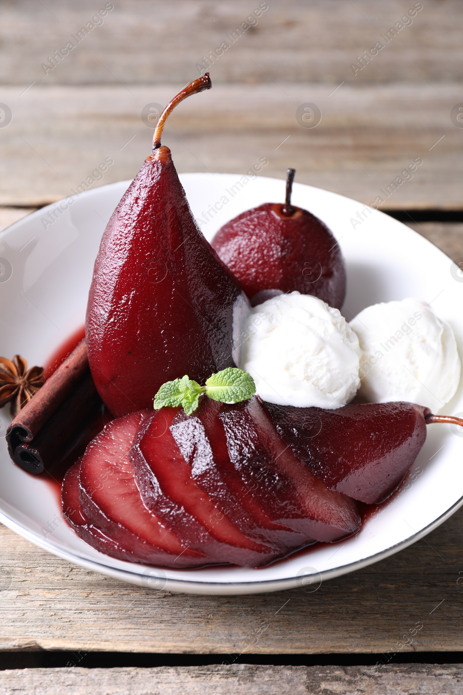 Photo of Tasty red wine poached pears and ice cream in bowl on wooden table, closeup