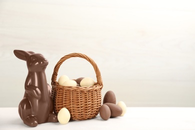 Photo of Chocolate Easter bunny and eggs on white table. Space for text