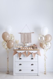 Photo of Baby shower party. Different delicious treats on white wooden chest of drawers and decor indoors
