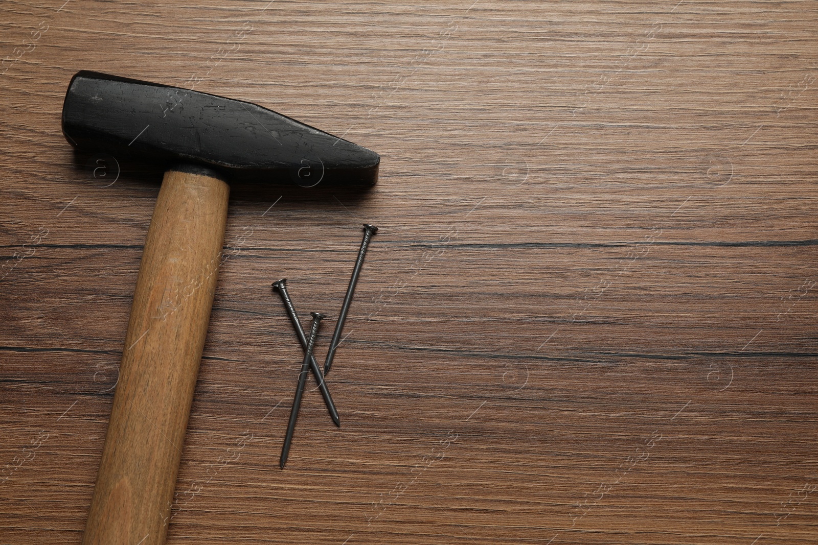 Photo of Hammer and metal nails on wooden table, top view. Space for text