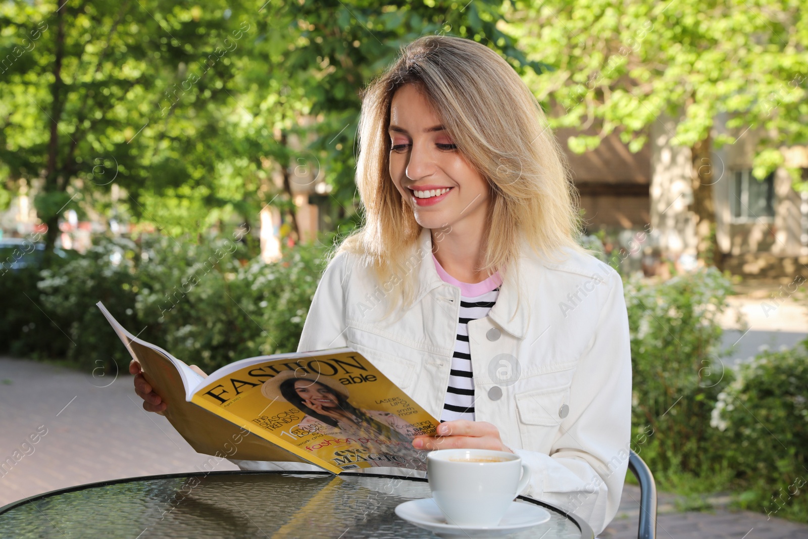 Photo of Happy young woman with cup of coffee and magazine enjoying early morning in outdoor cafe