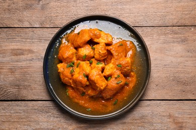 Plate of delicious chicken curry on wooden table, top view