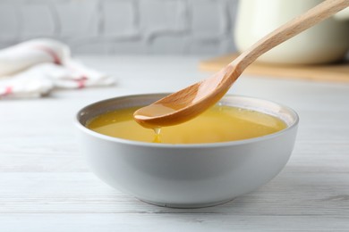 Photo of Spoon of clarified butter over bowl on white wooden table