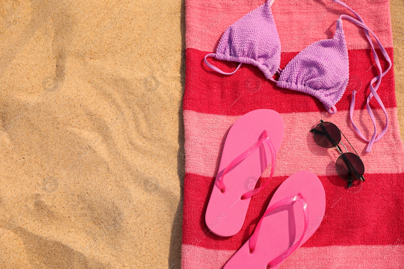 Photo of Beach towel with slippers, sunglasses and swimsuit on sand, top view. Space for text