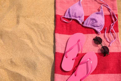 Beach towel with slippers, sunglasses and swimsuit on sand, top view. Space for text