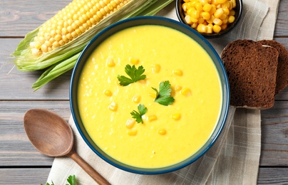 Photo of Delicious creamy corn soup served on wooden table, flat lay