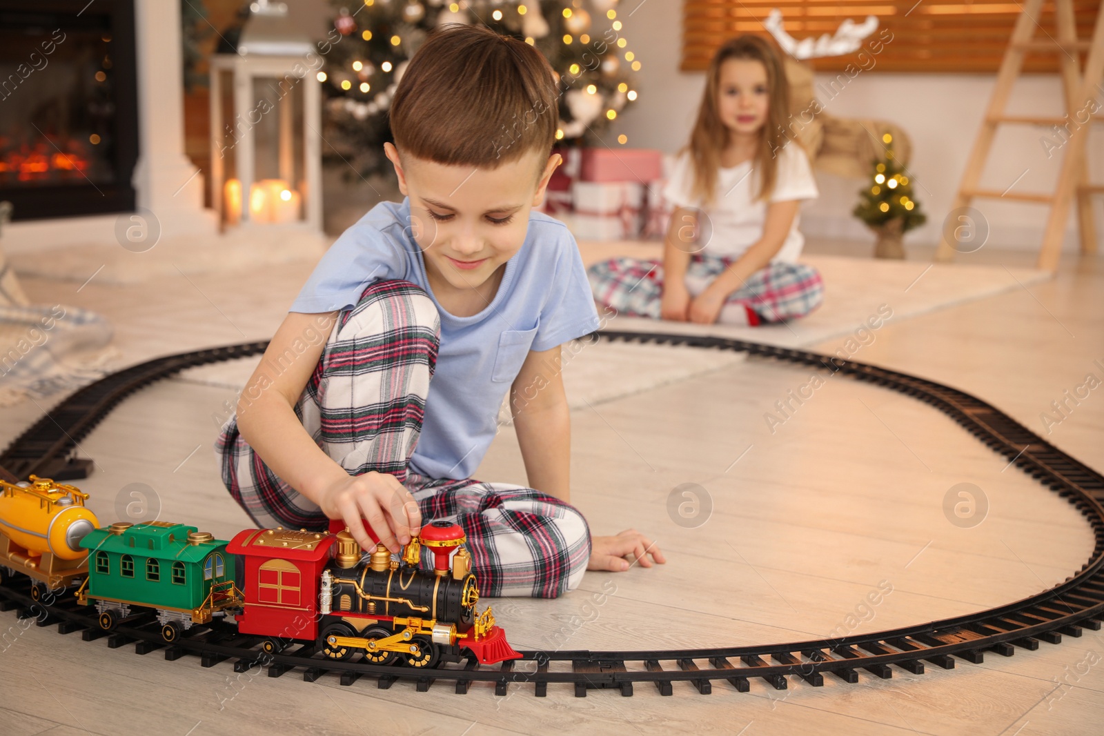 Photo of Children playing with colorful train toy in room decorated for Christmas