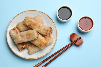 Fried spring rolls and sauces served on light blue table, top view