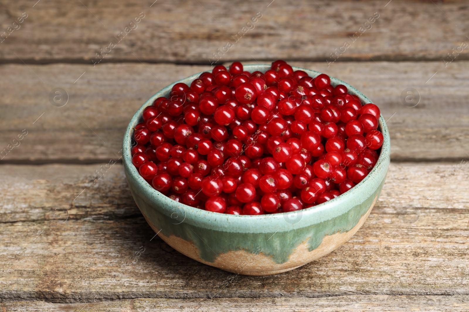 Photo of Ripe red currants in bowl on wooden table, closeup